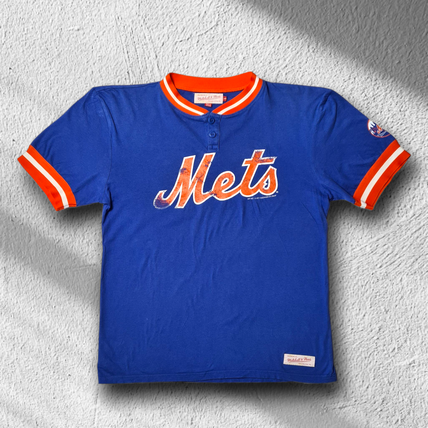 Mitchell & Ness New York Mets Shirt in Royalblau mit orangem Mets-Schriftzug und geripptem Kragen, Vorderansicht.