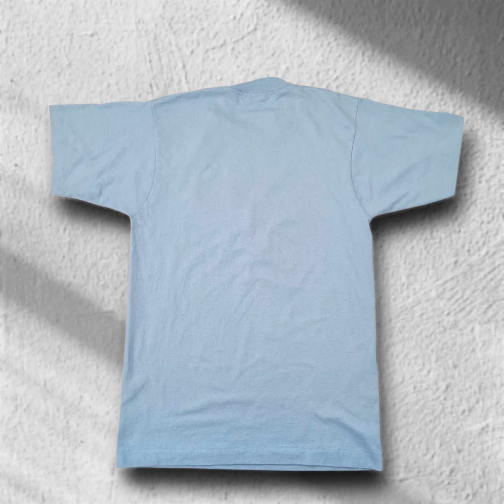 Rückansicht eines hellblauen Single Stitch Vintage T-Shirts, flach auf hellem Fliesenboden fotografiert.